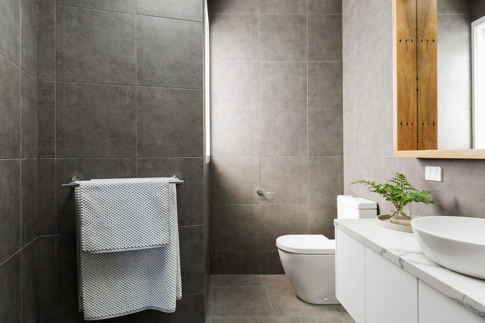 Cette image montre une salle de bain principale minimaliste de taille moyenne avec des portes de placard blanches, un carrelage gris, mosaïque, un mur gris, un sol en carrelage de céramique, une vasque, un plan de toilette en marbre, un sol gris et une cabine de douche à porte battante.