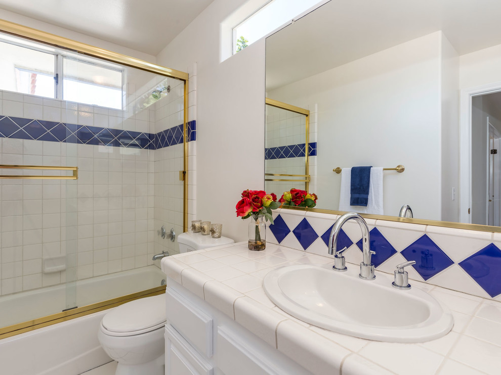 ロサンゼルスにある低価格の中くらいなトラディショナルスタイルのおしゃれな浴室 (フラットパネル扉のキャビネット、白いキャビネット、シャワー付き浴槽	、マルチカラーのタイル、セラミックタイル、タイルの洗面台、引戸のシャワー、アルコーブ型浴槽、一体型トイレ	、白い壁、セラミックタイルの床、オーバーカウンターシンク、白い床) の写真