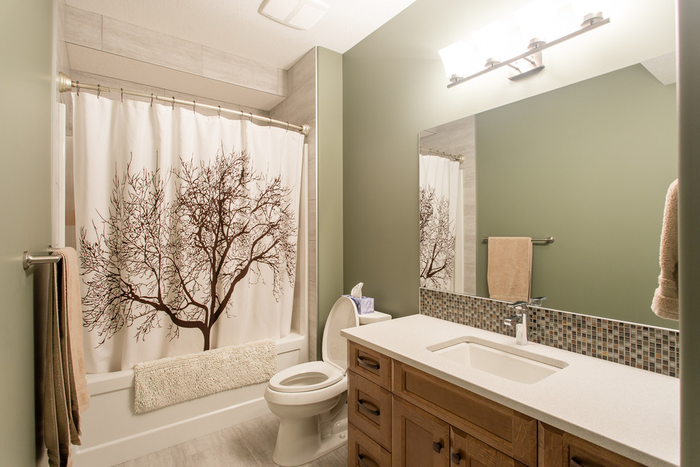 На фото: ванная комната среднего размера в классическом стиле с фасадами с утопленной филенкой, фасадами цвета дерева среднего тона, ванной в нише, душем над ванной, раздельным унитазом, разноцветной плиткой, плиткой из листового стекла, зелеными стенами, полом из керамогранита, душевой кабиной, врезной раковиной и столешницей из искусственного кварца
