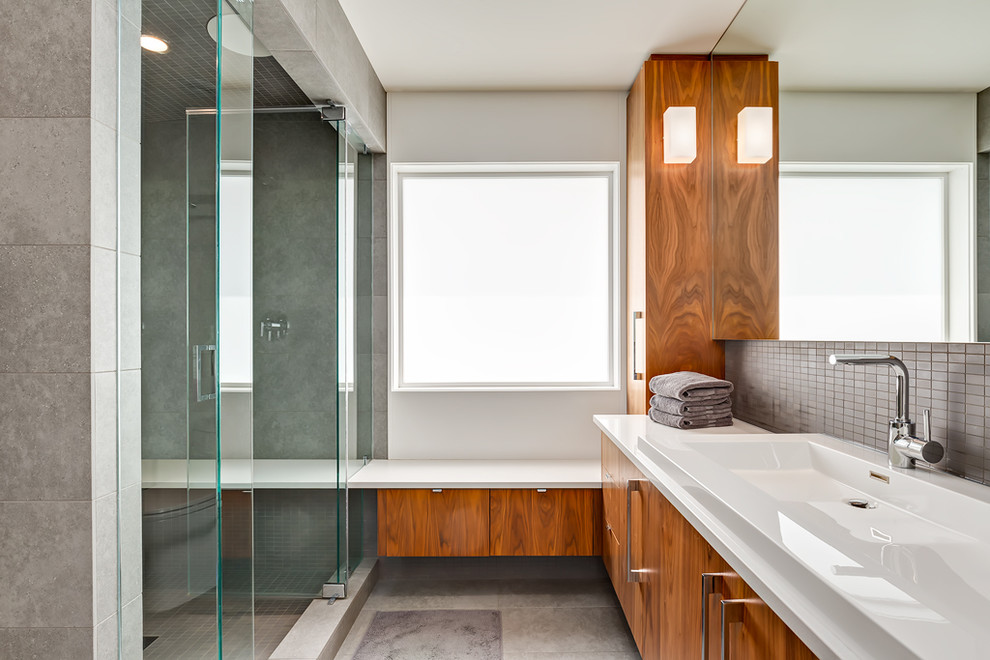 Cette image montre une salle de bain design avec un placard à porte plane, des portes de placard marrons, un mur blanc, un lavabo posé, un sol gris et une cabine de douche à porte battante.