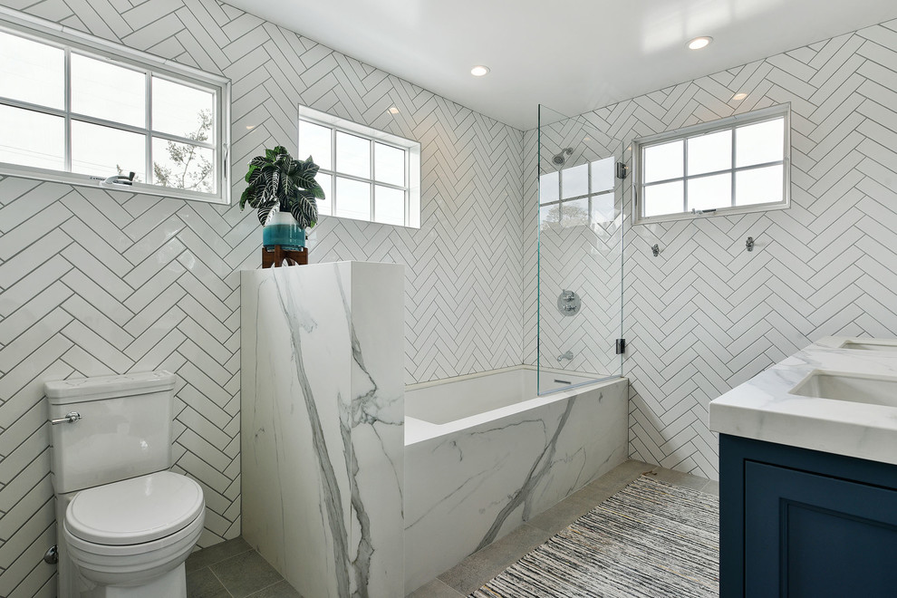 Exempel på ett mellanstort modernt vit vitt badrum med dusch, med luckor med infälld panel, blå skåp, ett badkar i en alkov, en dusch/badkar-kombination, en toalettstol med separat cisternkåpa, vit kakel, porslinskakel, vita väggar, betonggolv, ett undermonterad handfat, marmorbänkskiva, grått golv och med dusch som är öppen