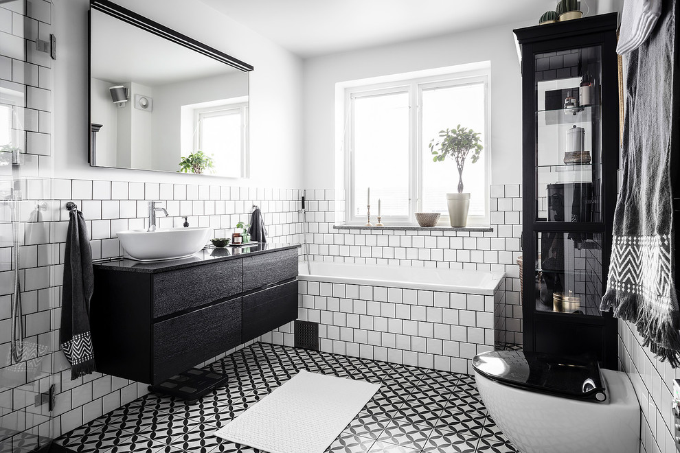 Inredning av ett skandinaviskt stort svart svart en-suite badrum, med en öppen dusch, en vägghängd toalettstol, vit kakel, keramikplattor, vita väggar, cementgolv, granitbänkskiva, flerfärgat golv, med dusch som är öppen, släta luckor, svarta skåp, ett hörnbadkar och ett fristående handfat