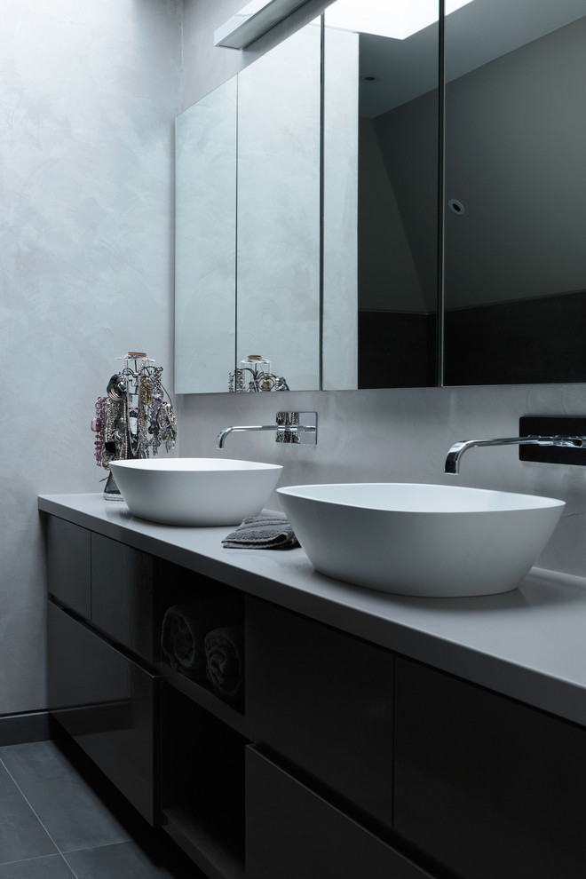 Réalisation d'une salle de bain principale design avec une vasque, des portes de placard noires et un mur gris.