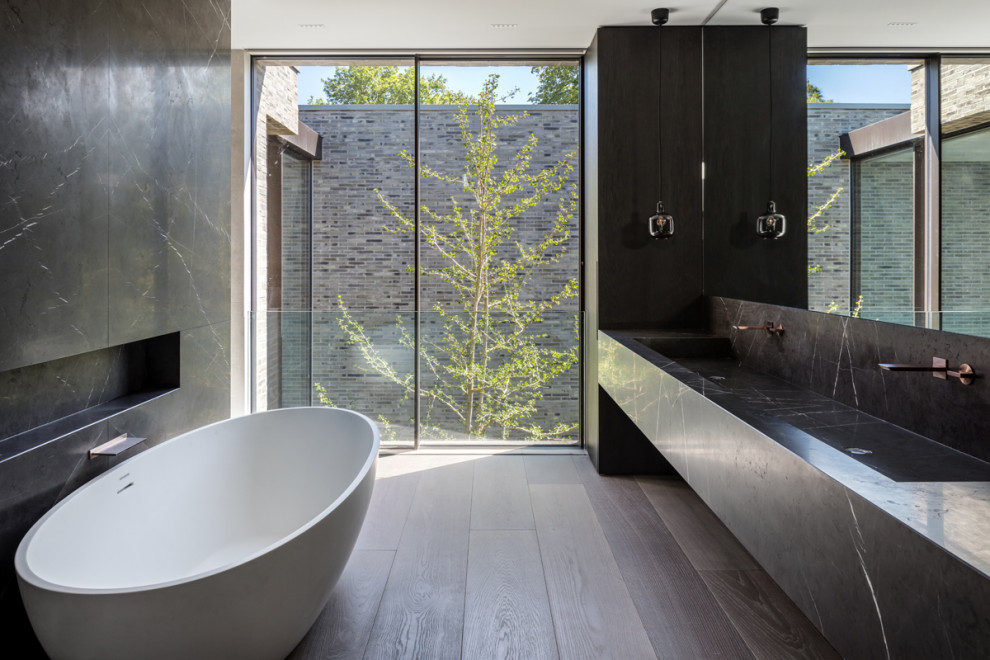 Modelo de cuarto de baño doble y flotante moderno con bañera exenta, suelo de madera oscura, lavabo de seno grande, suelo marrón, encimeras grises y hornacina