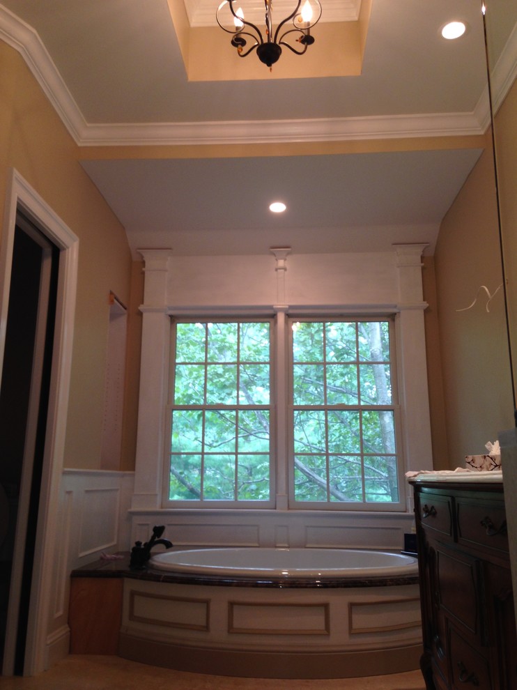 Cette image montre une salle de bain principale traditionnelle avec un lavabo encastré, un plan de toilette en marbre, une baignoire posée, WC séparés, un carrelage beige, un carrelage de pierre, un mur beige et un sol en travertin.