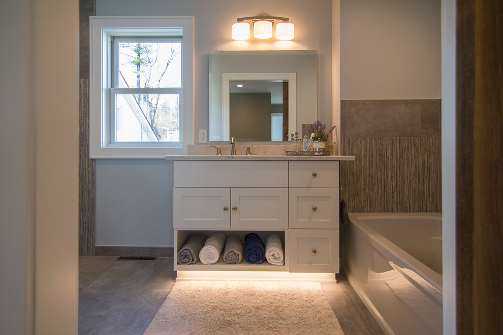 Cette image montre une douche en alcôve principale design de taille moyenne avec un placard à porte shaker, des portes de placard blanches, une baignoire en alcôve, WC séparés, un carrelage gris, des carreaux de porcelaine, un mur gris, un sol en vinyl, un lavabo encastré et un plan de toilette en granite.