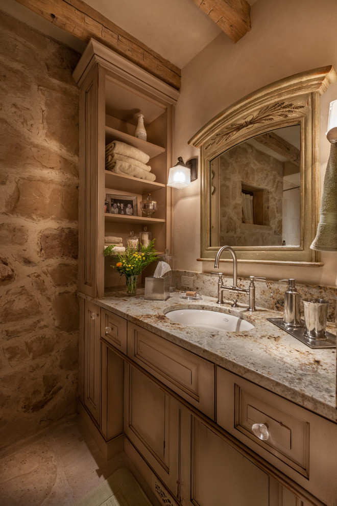 Idées déco pour une salle d'eau classique en bois vieilli de taille moyenne avec un placard avec porte à panneau surélevé, un lavabo encastré, un carrelage beige, un mur beige, un sol en carrelage de porcelaine, un plan de toilette en granite et un mur en pierre.