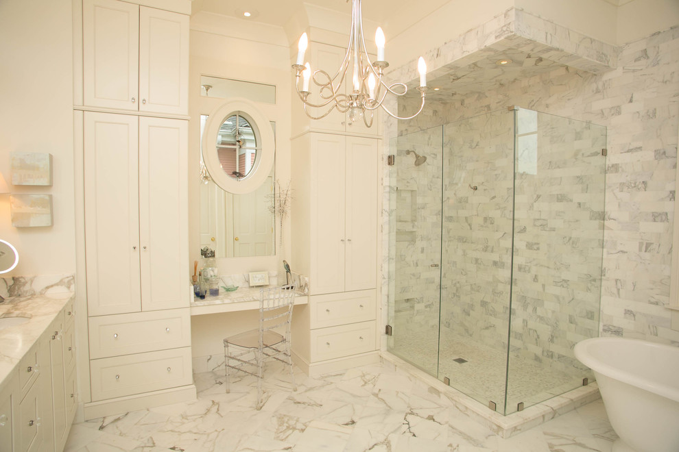 This is an example of a large traditional ensuite bathroom in New Orleans with a submerged sink, recessed-panel cabinets, white cabinets, marble worktops, a freestanding bath, stone tiles, white walls and marble flooring.