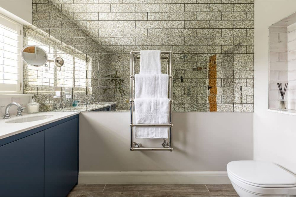 Inspiration pour une salle de bain design avec un placard à porte plane, des portes de placard bleues, une baignoire indépendante, WC suspendus, un carrelage beige, des carreaux de miroir, un mur beige, un sol en carrelage de porcelaine, un sol gris, un plan de toilette en surface solide, un plan de toilette blanc et un lavabo encastré.