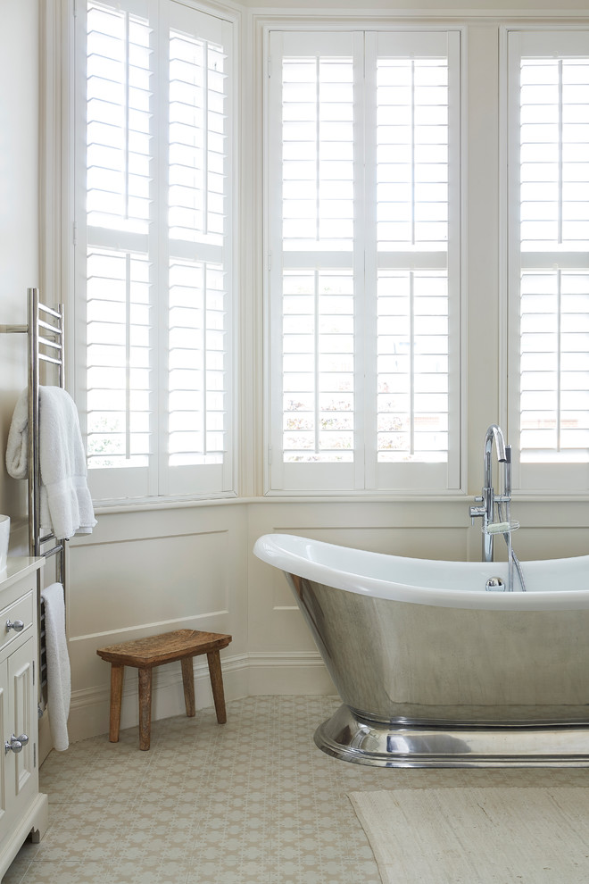 Imagen de cuarto de baño clásico con puertas de armario beige, bañera exenta, baldosas y/o azulejos blancos, baldosas y/o azulejos en mosaico, paredes blancas y suelo con mosaicos de baldosas