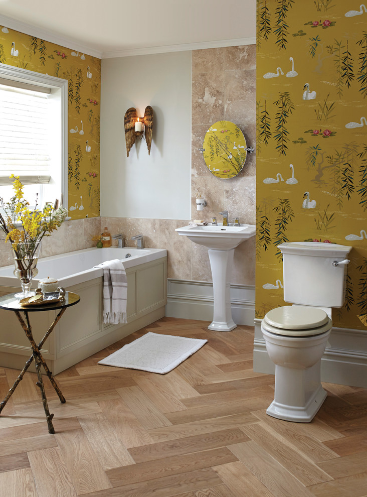 Inredning av ett klassiskt badrum, med ett platsbyggt badkar, en toalettstol med separat cisternkåpa, beige kakel, gula väggar, ett piedestal handfat och mellanmörkt trägolv