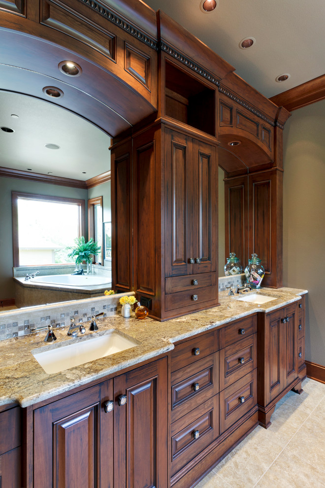 Cette image montre une salle de bain traditionnelle en bois foncé avec un lavabo encastré, un placard avec porte à panneau surélevé, un plan de toilette en granite, un carrelage beige et mosaïque.