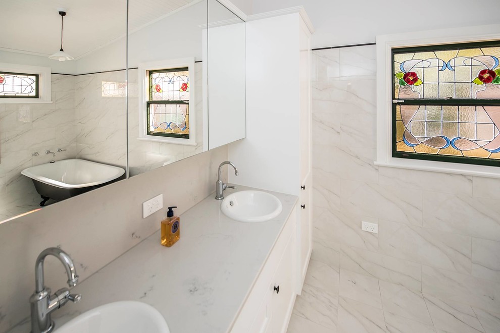 На фото: главная ванная комната среднего размера в классическом стиле с отдельно стоящей ванной, унитазом-моноблоком, белой плиткой, мраморной плиткой, белыми стенами, мраморным полом, белым полом, душем с распашными дверями, фасадами с утопленной филенкой, белыми фасадами, душем в нише, накладной раковиной, мраморной столешницей, белой столешницей, тумбой под две раковины и встроенной тумбой