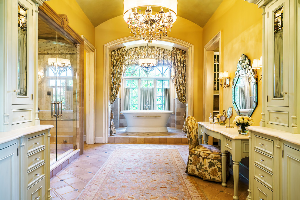 Klassisk inredning av ett mycket stort en-suite badrum, med skåp i ljust trä, beige kakel, gula väggar, klinkergolv i porslin, marmorbänkskiva, ett fristående badkar, en dusch i en alkov, dusch med gångjärnsdörr och luckor med profilerade fronter