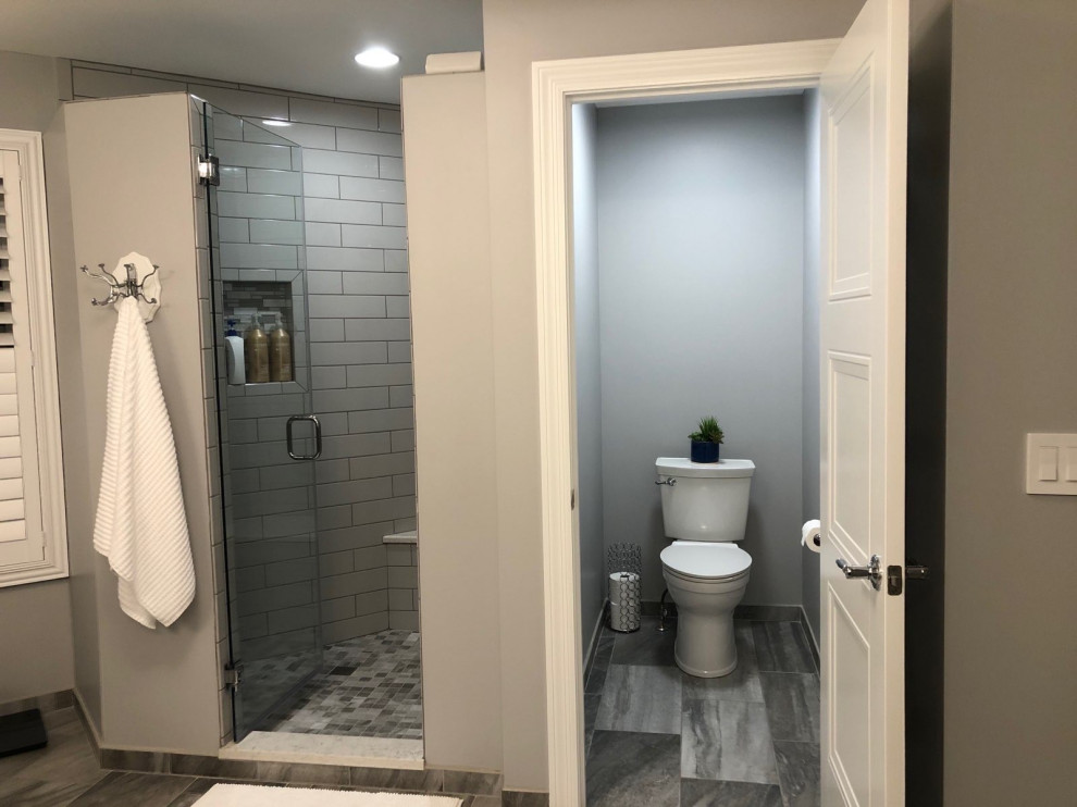 Design ideas for a large traditional ensuite bathroom in St Louis with recessed-panel cabinets, grey cabinets, a freestanding bath, an alcove shower, a two-piece toilet, white tiles, metro tiles, grey walls, a submerged sink, grey floors, a hinged door, grey worktops, a wall niche, a shower bench, an enclosed toilet and a built in vanity unit.