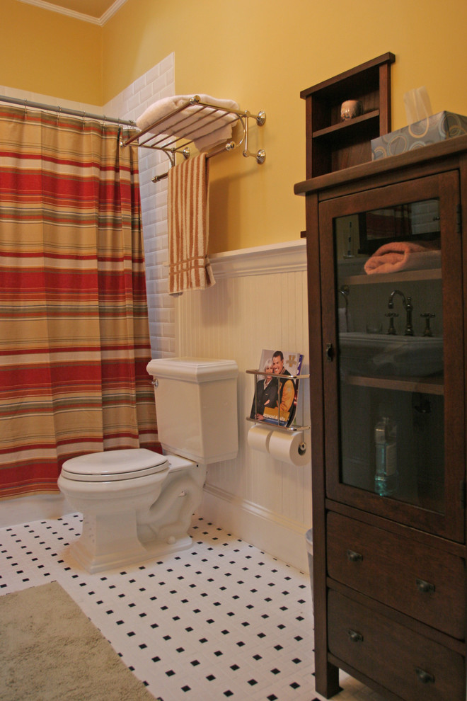 Klassisches Badezimmer mit dunklen Holzschränken, gelber Wandfarbe, Badewanne in Nische, Duschbadewanne, weißen Fliesen, Metrofliesen und Sockelwaschbecken in Atlanta