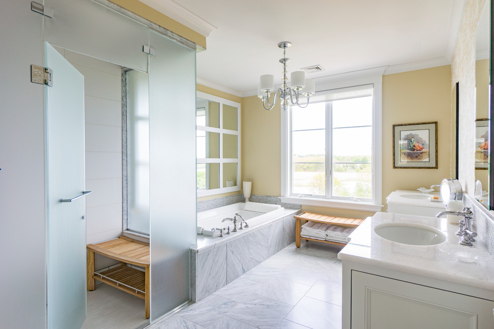 Exemple d'une salle de bain principale et grise et jaune chic avec une baignoire posée, un espace douche bain, un carrelage blanc, un mur jaune, un lavabo encastré, un sol gris et une cabine de douche à porte battante.