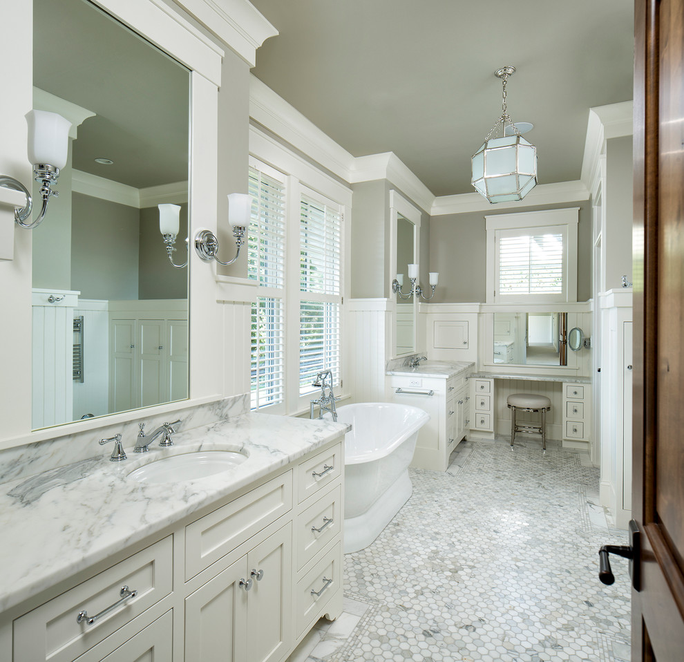 Inredning av ett klassiskt en-suite badrum, med skåp i shakerstil, vita skåp, ett fristående badkar, vit kakel, mosaik, grå väggar, ett undermonterad handfat och marmorbänkskiva