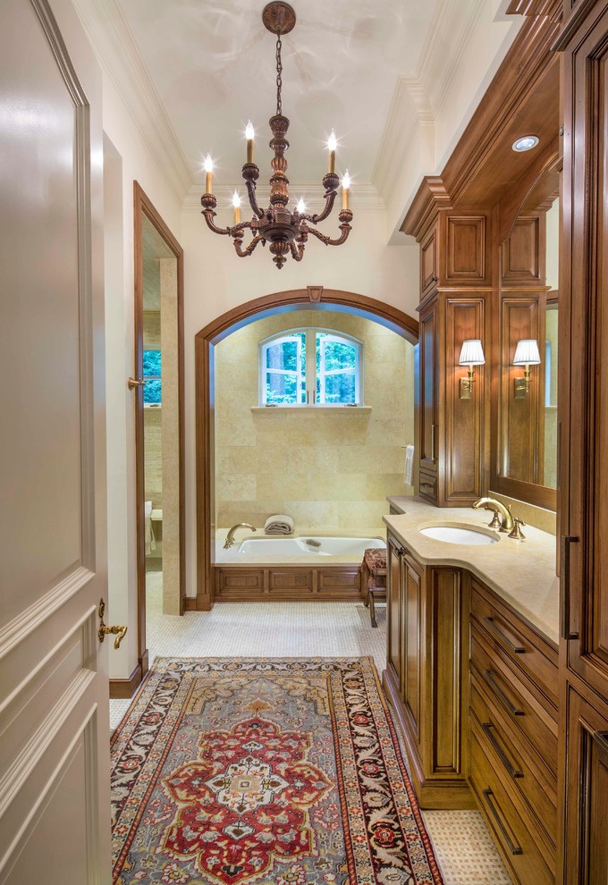 Réalisation d'une salle de bain tradition en bois foncé avec un lavabo encastré, un placard avec porte à panneau surélevé, une baignoire encastrée, un carrelage beige, un mur beige et un sol en carrelage de terre cuite.