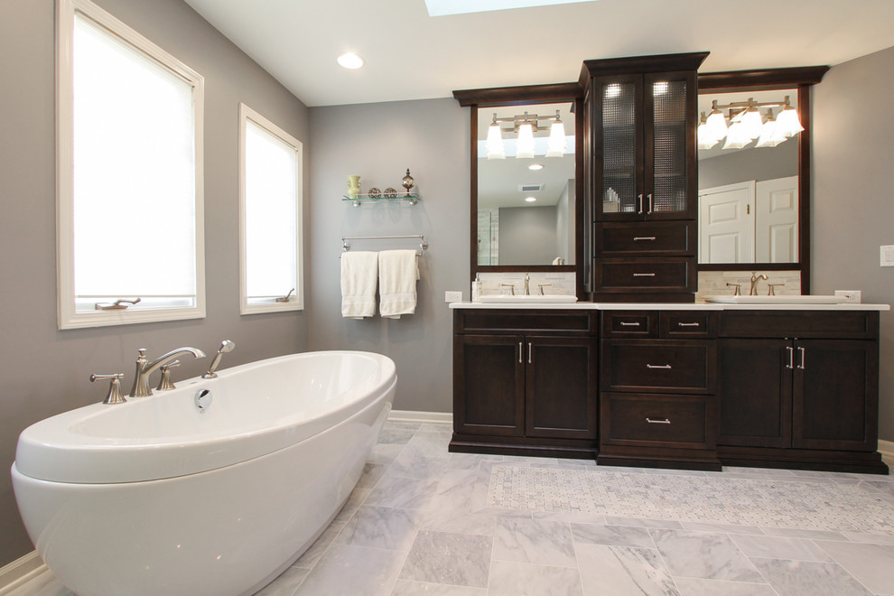 This is an example of a large classic ensuite bathroom in Chicago with a built-in sink, dark wood cabinets, a freestanding bath, white tiles, grey tiles, multi-coloured tiles, stone tiles, grey walls, marble flooring, shaker cabinets, a corner shower and engineered stone worktops.