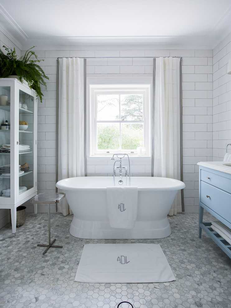 Aménagement d'une salle de bain principale classique avec un placard avec porte à panneau encastré, des portes de placard bleues, une baignoire indépendante, WC suspendus, un carrelage gris, mosaïque, un mur blanc, un sol en marbre, un lavabo encastré et un plan de toilette en marbre.