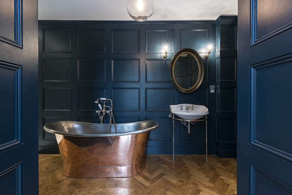 Foto på ett vintage badrum, med ett konsol handfat, ett fristående badkar, blå väggar och mörkt trägolv