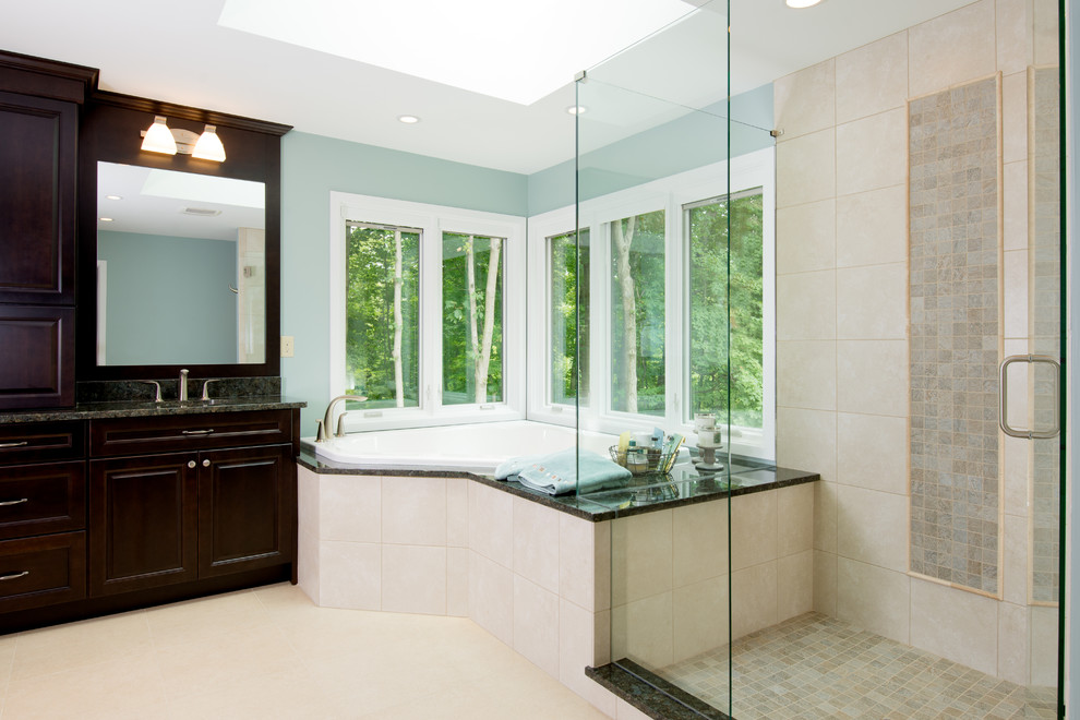 This is an example of a medium sized classic ensuite bathroom in Cincinnati with raised-panel cabinets, dark wood cabinets, a corner bath, a corner shower, a one-piece toilet, beige tiles, blue walls, a submerged sink, granite worktops, porcelain tiles, porcelain flooring, beige floors and a hinged door.
