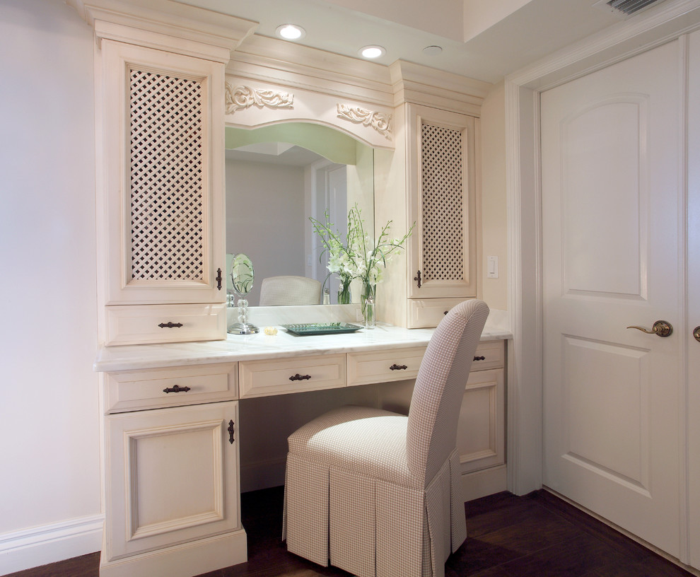 Modelo de cuarto de baño tradicional de tamaño medio con armarios con paneles empotrados, puertas de armario beige, paredes púrpuras, suelo de madera oscura, encimera de mármol, suelo marrón y encimeras blancas