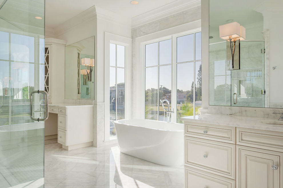 Großes Klassisches Badezimmer En Suite mit weißer Wandfarbe, Marmorboden, Unterbauwaschbecken, weißem Boden, profilierten Schrankfronten, weißen Schränken, freistehender Badewanne, Waschtisch aus Holz, Falttür-Duschabtrennung und Marmorfliesen in Tampa