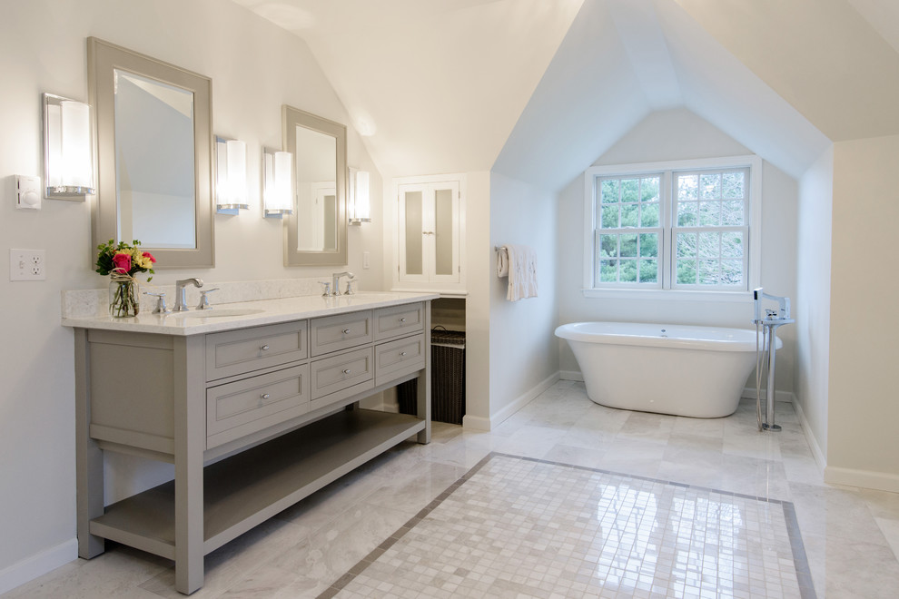 На фото: большая главная ванная комната в классическом стиле с фасадами с утопленной филенкой, серыми фасадами, отдельно стоящей ванной, серой плиткой, каменной плиткой и мраморной столешницей с
