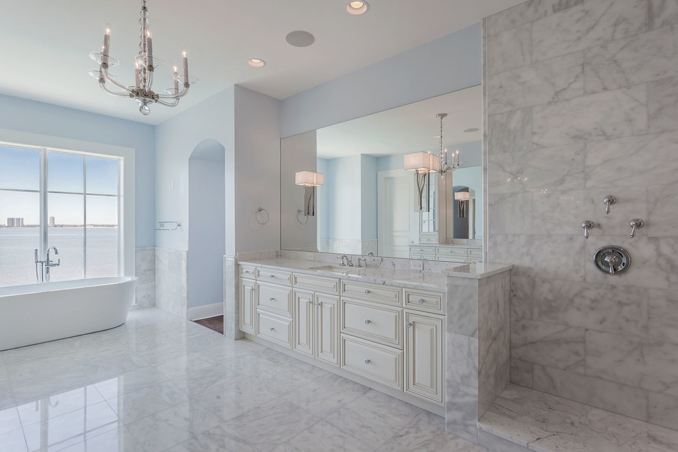 Inspiration for a large classic ensuite bathroom in Tampa with raised-panel cabinets, white cabinets, a freestanding bath, grey tiles, white tiles, marble tiles, blue walls, marble flooring, a submerged sink, quartz worktops and white floors.