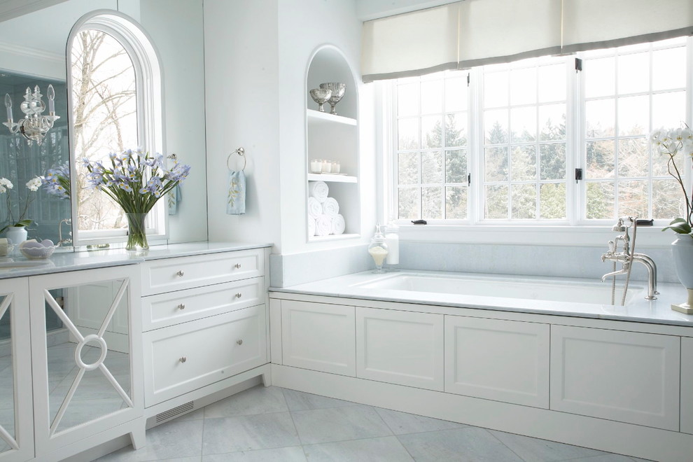 Aménagement d'une salle de bain principale classique avec des portes de placard blanches, une baignoire posée, un carrelage gris, un carrelage de pierre, un sol en marbre, un plan de toilette en marbre, un mur bleu et un placard avec porte à panneau encastré.