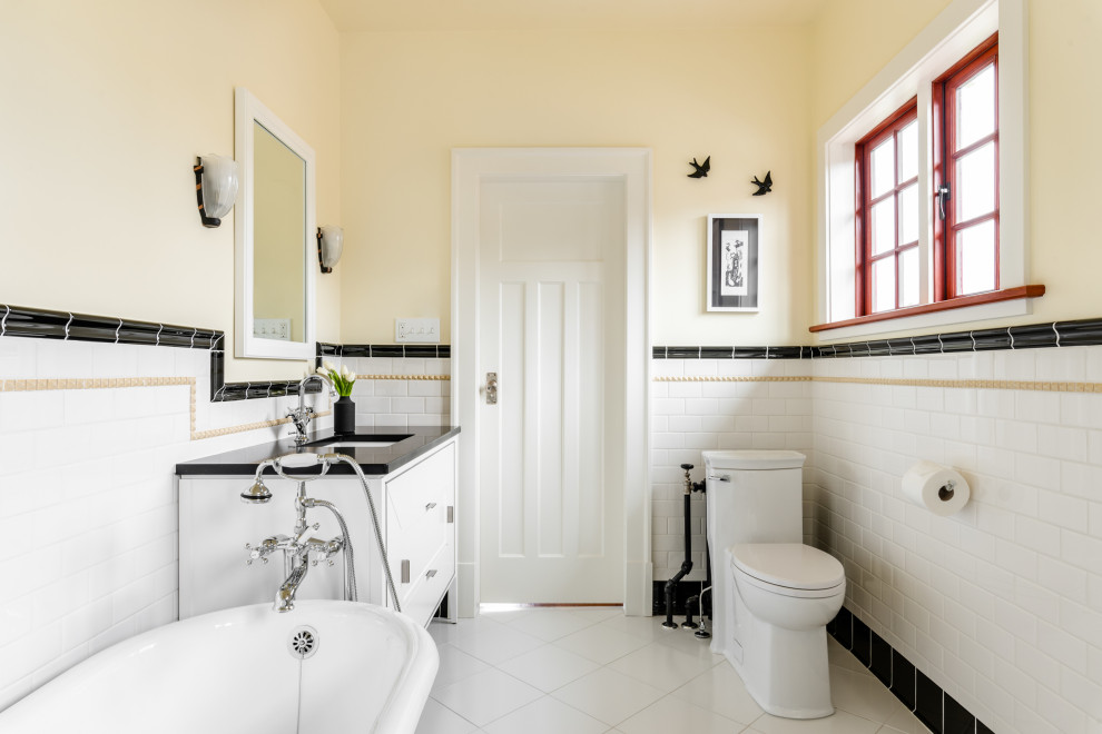 На фото: большая главная ванная комната в классическом стиле с фасадами островного типа, белыми фасадами, ванной на ножках, угловым душем, унитазом-моноблоком, разноцветной плиткой, керамической плиткой, желтыми стенами, полом из керамической плитки, врезной раковиной, столешницей из искусственного кварца, белым полом, душем с распашными дверями и черной столешницей с