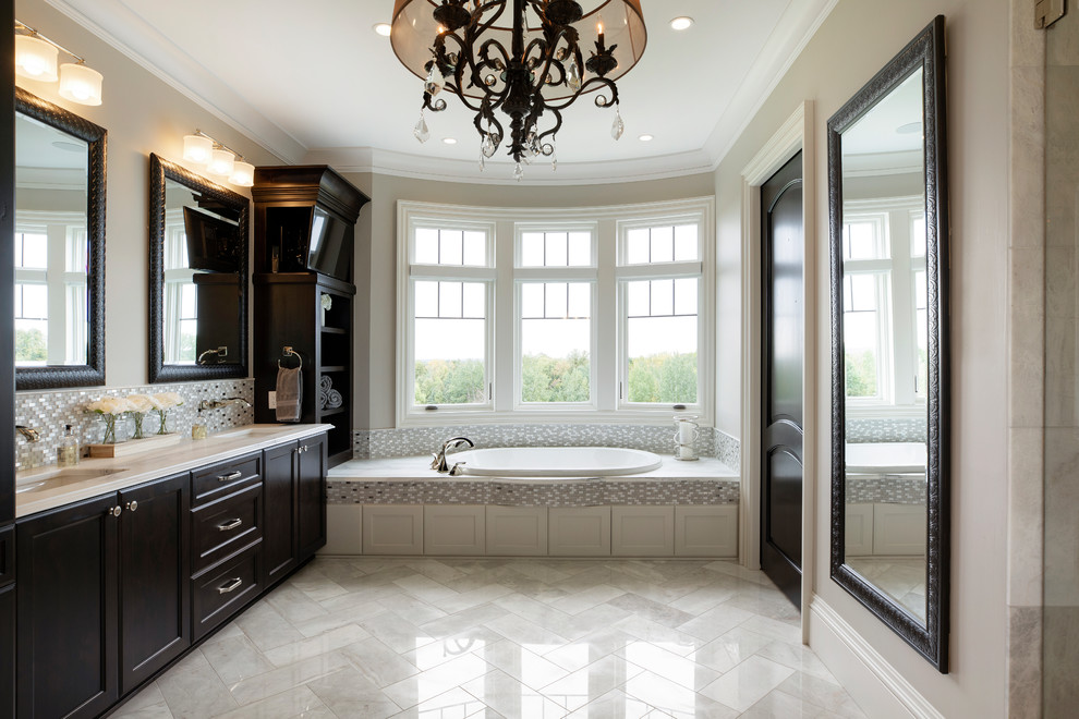 Photo of an expansive traditional ensuite bathroom in Minneapolis with recessed-panel cabinets, dark wood cabinets, a built-in bath, an alcove shower, a one-piece toilet, grey tiles, porcelain tiles, grey walls, porcelain flooring, a submerged sink, granite worktops and white worktops.