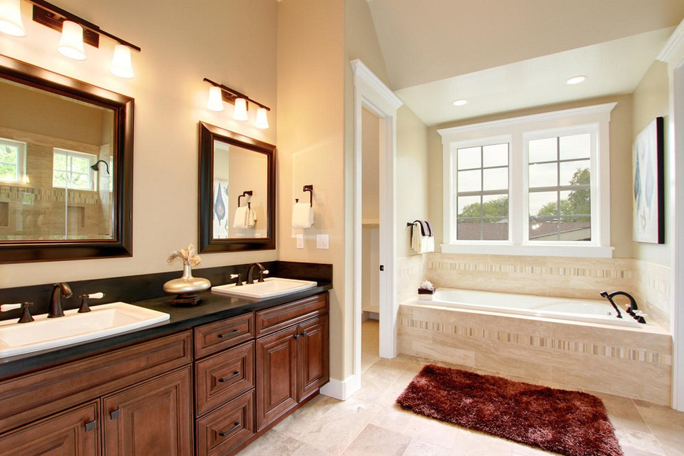Immagine di una grande stanza da bagno padronale tradizionale con ante con bugna sagomata, ante in legno bruno, vasca da incasso, piastrelle beige e lavabo da incasso