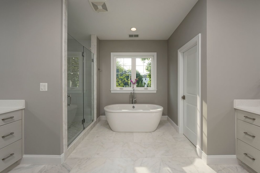 Klassisk inredning av ett mellanstort badrum med dusch, med luckor med profilerade fronter, grå skåp, ett fristående badkar, en dusch i en alkov, en toalettstol med hel cisternkåpa, grå väggar, marmorgolv och ett undermonterad handfat