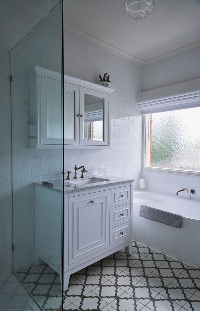 Klassisk inredning av ett litet grå grått en-suite badrum, med skåp i shakerstil, vita skåp, ett fristående badkar, en hörndusch, en toalettstol med hel cisternkåpa, vit kakel, keramikplattor, vita väggar, klinkergolv i keramik, ett integrerad handfat, marmorbänkskiva, beiget golv och dusch med gångjärnsdörr
