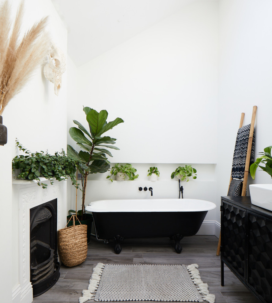 This is an example of a traditional bathroom in Sussex with flat-panel cabinets, black cabinets, a claw-foot bath, white walls, a vessel sink, grey floors, black worktops, a wall niche, a chimney breast, a freestanding vanity unit and a vaulted ceiling.