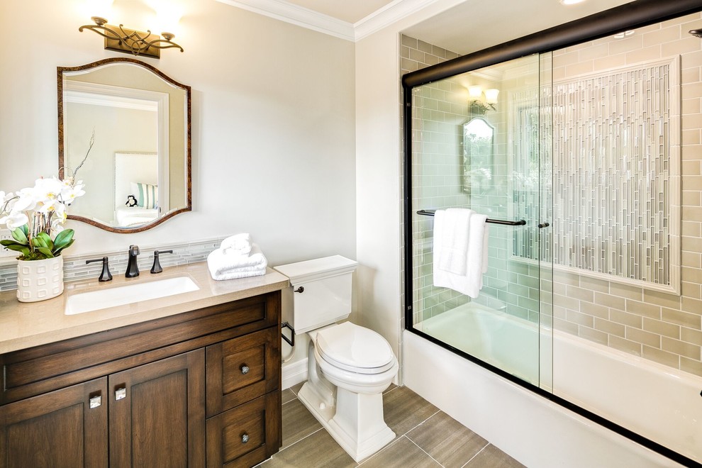 Photo of a medium sized traditional shower room bathroom in Orange County with recessed-panel cabinets, dark wood cabinets, an alcove bath, a shower/bath combination, a one-piece toilet, beige tiles, porcelain tiles, beige walls, porcelain flooring, a submerged sink, engineered stone worktops, beige floors and a sliding door.