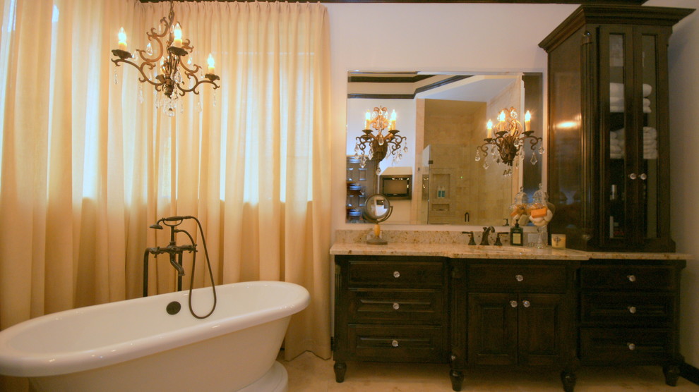 На фото: ванная комната в классическом стиле с врезной раковиной, фасадами островного типа, темными деревянными фасадами, столешницей из гранита, отдельно стоящей ванной, угловым душем, раздельным унитазом, бежевой плиткой и каменной плиткой
