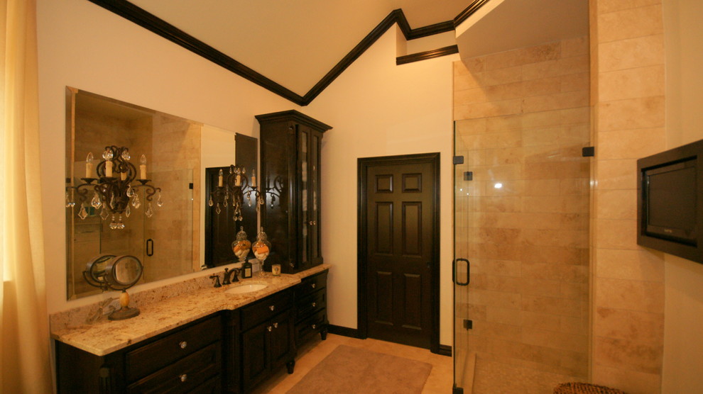 На фото: ванная комната в классическом стиле с врезной раковиной, фасадами островного типа, темными деревянными фасадами, столешницей из гранита, отдельно стоящей ванной, угловым душем, раздельным унитазом, бежевой плиткой и каменной плиткой с