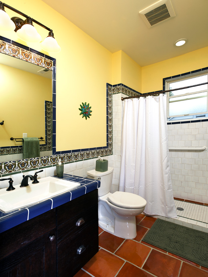 Foto på ett mellanstort medelhavsstil badrum, med ett nedsänkt handfat, luckor med upphöjd panel, skåp i mörkt trä, kaklad bänkskiva, en dusch i en alkov, en toalettstol med separat cisternkåpa, blå kakel, keramikplattor, vita väggar och klinkergolv i porslin