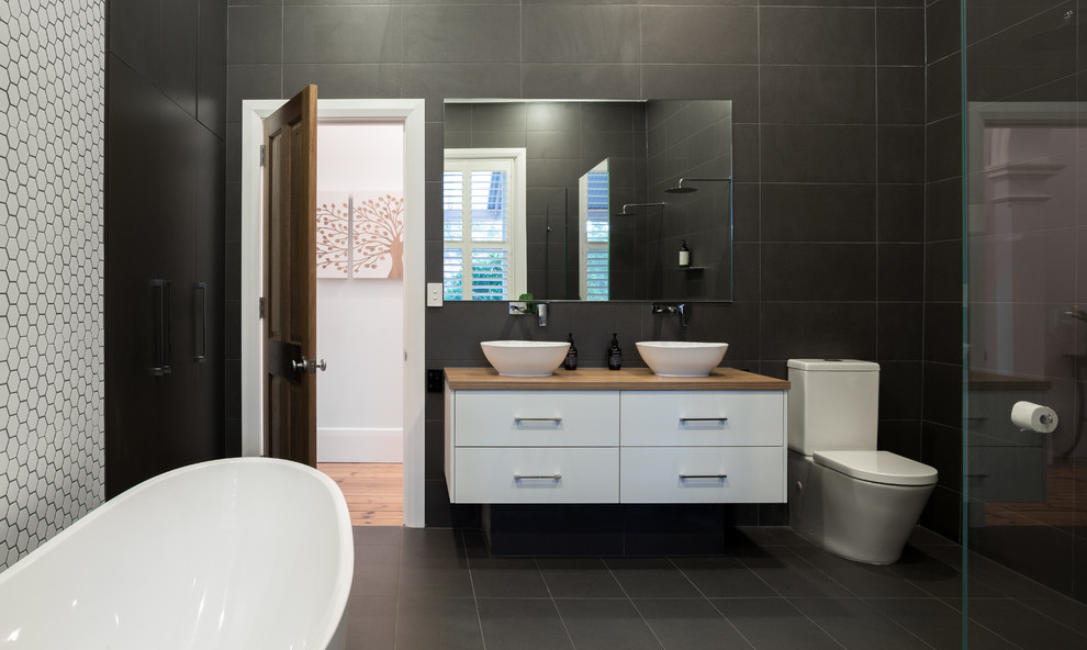 Пример оригинального дизайна: большая ванная комната в современном стиле с отдельно стоящей ванной, двойным душем, черно-белой плиткой, полом из керамической плитки и подвесной раковиной