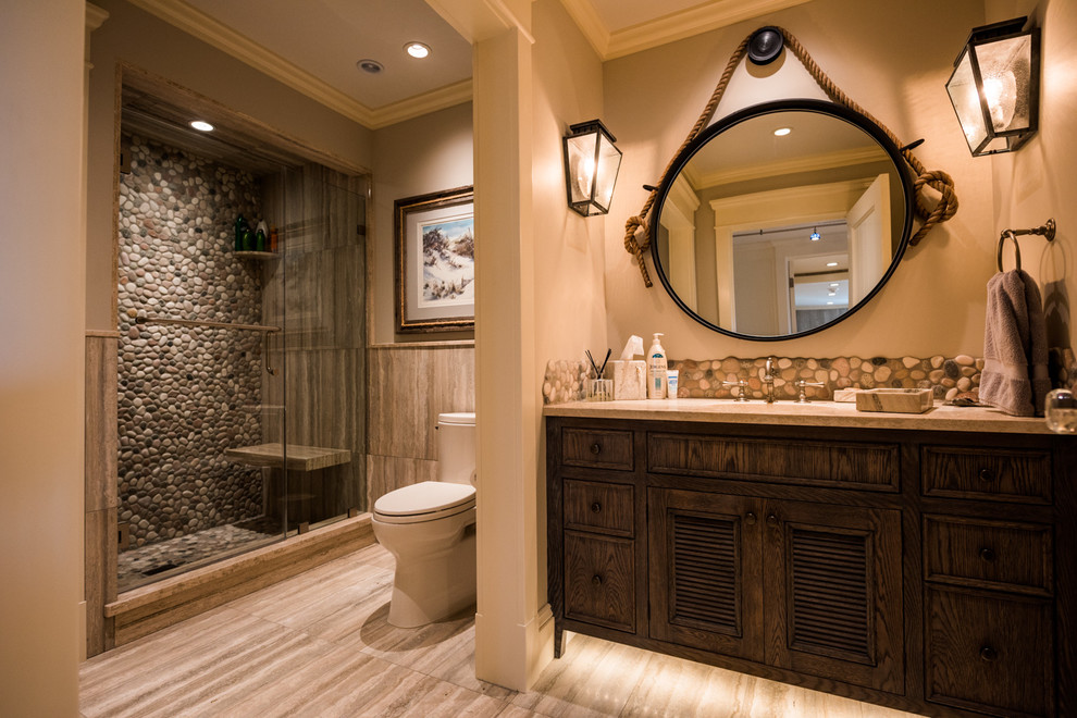 Cette image montre une salle de bain chalet en bois foncé de taille moyenne avec un placard à porte affleurante, WC séparés, un carrelage beige, une plaque de galets, un mur beige, un sol en carrelage de céramique, un lavabo encastré et un plan de toilette en granite.