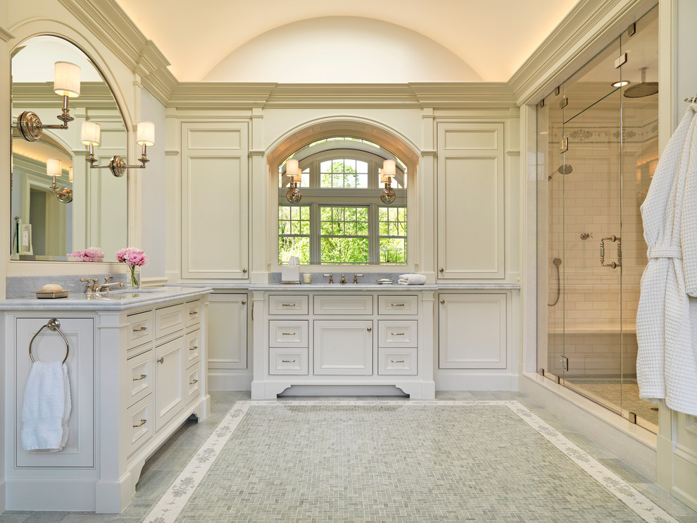 Klassisk inredning av ett badrum, med ett undermonterad handfat, luckor med profilerade fronter, vita skåp, marmorbänkskiva, en dusch i en alkov och vit kakel
