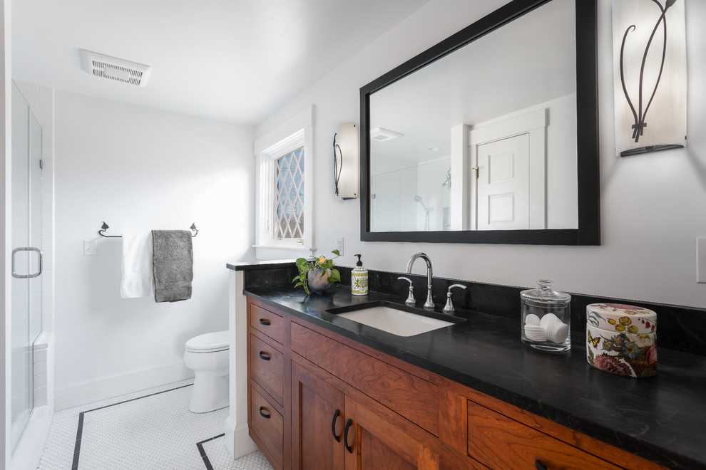Mid-sized elegant master white tile and ceramic tile porcelain tile and white floor alcove shower photo in Boston with flat-panel cabinets, medium tone wood cabinets, a one-piece toilet, white walls, an undermount sink, soapstone countertops, a hinged shower door and black countertops