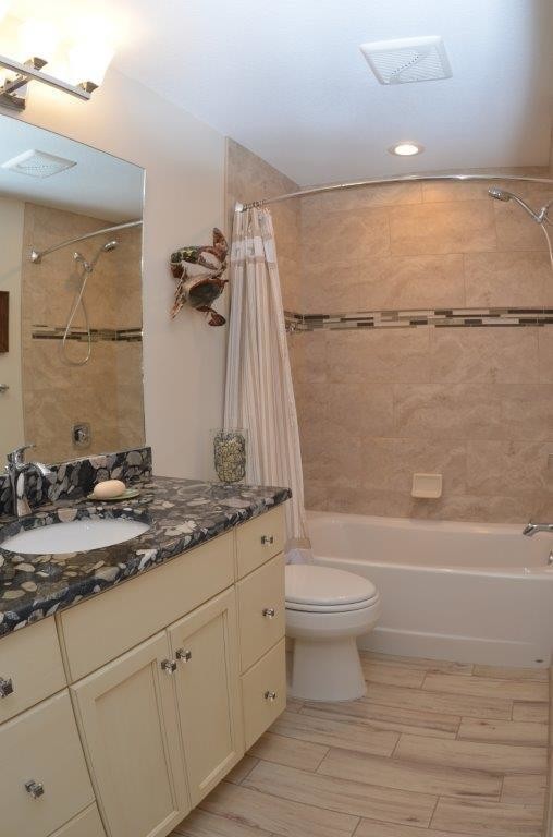 Exemple d'une salle d'eau chic de taille moyenne avec un placard à porte plane, des portes de placard beiges, une baignoire en alcôve, un combiné douche/baignoire, WC à poser, un mur beige, un sol en carrelage de porcelaine, un lavabo encastré et un plan de toilette en onyx.