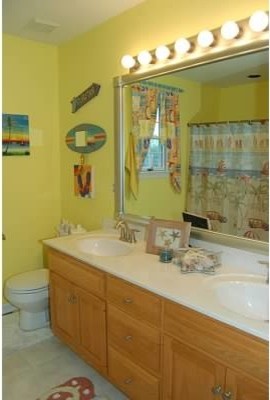 Inredning av ett maritimt mellanstort badrum för barn, med luckor med upphöjd panel, skåp i ljust trä, ett badkar i en alkov, en toalettstol med separat cisternkåpa, gula väggar, vinylgolv, ett integrerad handfat och bänkskiva i akrylsten