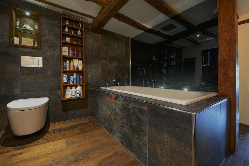 Inspiration for a large rural ensuite bathroom in Kent with a trough sink, open cabinets, dark wood cabinets, wooden worktops, a walk-in shower, a wall mounted toilet, grey tiles, ceramic tiles, beige walls and dark hardwood flooring.