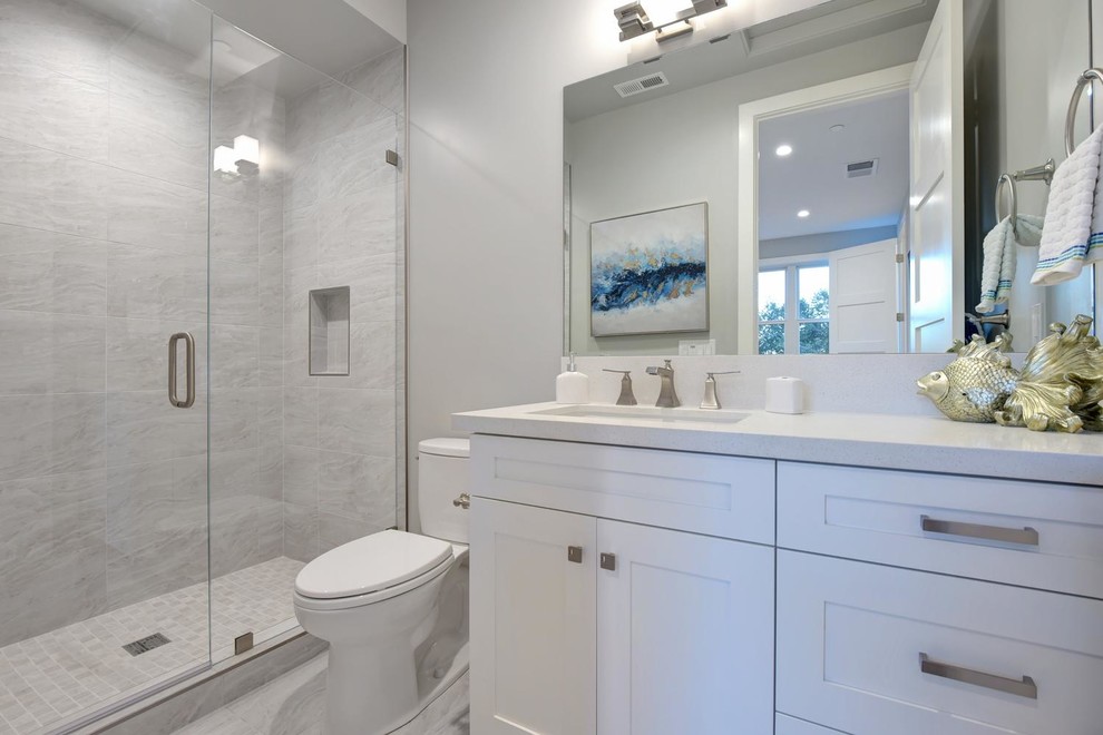 Inredning av ett klassiskt stort vit vitt badrum med dusch, med skåp i shakerstil, vita skåp, en dusch i en alkov, grå kakel, grå väggar, ett undermonterad handfat, grått golv, dusch med gångjärnsdörr, en toalettstol med hel cisternkåpa, porslinskakel, klinkergolv i porslin och bänkskiva i kvarts
